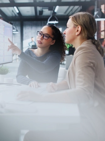Two women in an office setting, looking at a computer monitor displaying data on EUC remediation, with one woman pointing at the screen.